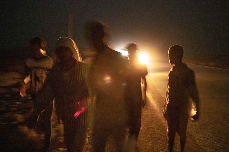 In this July 12, 2019 photo, 35-year-old Mohammed Eissa, second left, walks on a highway with boys he met on the way, around 50 kilometers (31 miles) from Djibouti. Eissa had left behind his wife, nine sons and a daughter. His wife cares for his elderly father. The children work the farm growing vegetables, but harvests are unpredictable: "If there's no rain, there's nothing." (AP Photo/Nariman El-Mofty)