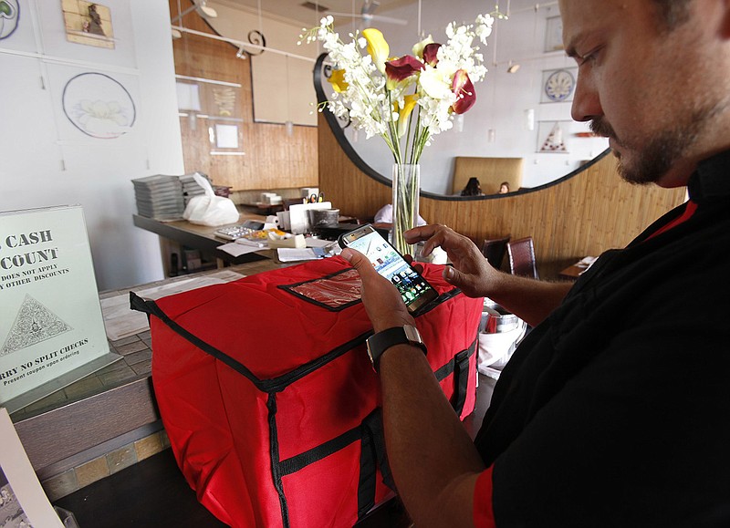 Sergio Reyes of DoorDash takes note of the order in front of him and relays a message to the client that he is on his way. (John Gastaldo/San Diego Union-Tribune/TNS)