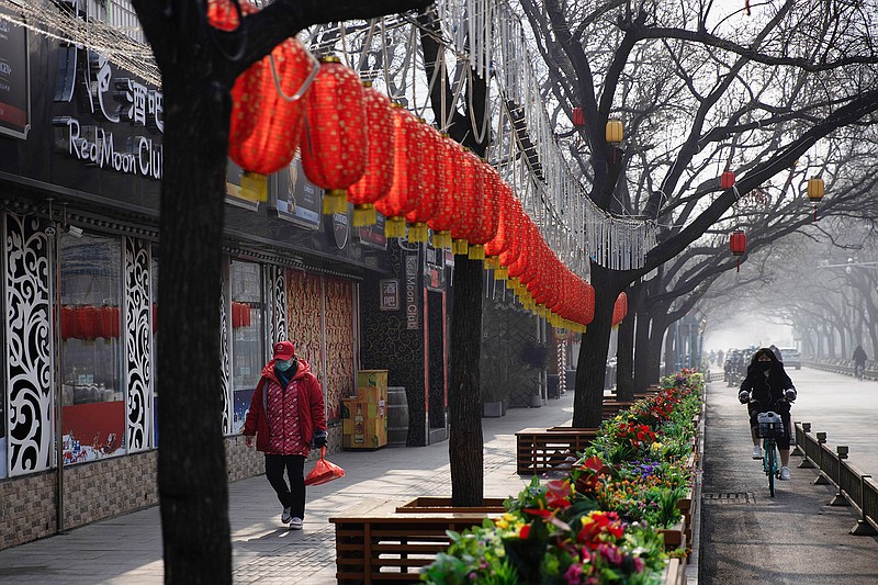 In this photo taken Tuesday, Feb. 11, 2020, a woman walks past Lunar New Year decor and shuttered bars at a retail district in Beijing, China. Millions of Chinese workers and entrepreneurs are bearing the rising costs of an anti-virus campaign that has shut down large sections of the economy. The government has imposed restrictions nationwide that have stalled travel and sales of real estate and autos. (AP Photo/Ng Han Guan)