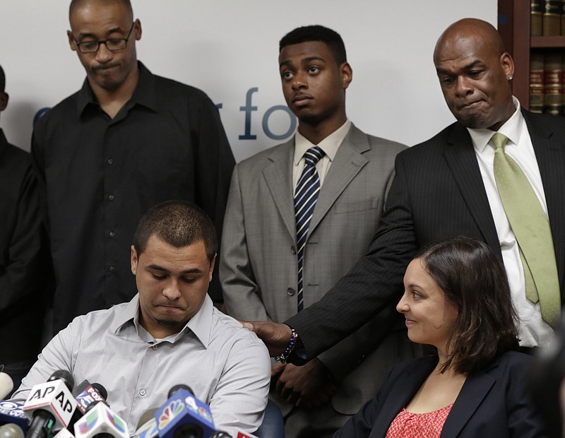 FILE - In this Aug. 12, 2013 file photo, plaintiff in the stop and frisk case David Ourlicht, seated left, is comforted by Merault Almonar, standing at right, father of plaintiff Devin Almonar, standing center, during a news conference at the Center for Constitutional Rights, in New York, after . U.S. District Judge Shira Scheindlin ruled that the New York Police Department deliberately violated the civil rights of tens of thousands of New Yorkers with its contentious stop-and-frisk policy. Standing at left is plaintiff Leroy Downes while attorney Jenn Borchetta listens, seated right. (AP Photo/Richard Drew, File)