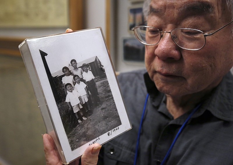 In this photo taken Tuesday, Feb. 11, 2020, Les Ouchida holds a 1943 photo of himself, front row, center, and his siblings taken at the internment camp his family was moved to, as he poses at the permanent exhibit titled "UpRooted Japanese Americans in World War II" at the California Museum in Sacramento, Calif. Ochida, who is a docent for the exhibit, and his family were forced to move in 1942 from their home near Sacramento to a camp in Jerome, Arkansas. Assemblyman Al Muratsuchi, D-Torrence has introduced a resolution to apologize for the state's role in carrying out the federal government's internment of Japanese-Americans. A similar resolution will be brought up before the state Senate by Sen. Richard Pan, D-Sacramento.(AP Photo/Rich Pedroncelli)