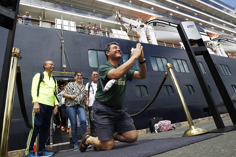 ADDS NAME OF PASSENGER - FILE - In this Feb. 14, 2020, file photo, John Miller, from Orcas Island, Wash., reacts after he disembarked from the MS Westerdam, back, at the port of Sihanoukville, Cambodia. Having finally reached a friendly port willing to accept them and stepped ashore after weeks of uncertainty at sea, hundreds of cruise ship passengers eyed warily over fears of a new virus are now simply trying to find a way home. (AP Photo/Heng Sinith, File)