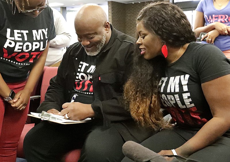 FILE- In this Jan. 8, 2019 file photo, former felon Desmond Meade and president of the Florida Rights Restoration Coalition, left, fills out a voter registration form as his wife Sheena looks on at the Supervisor of Elections office in Orlando, Fla. On Wednesday, Feb. 19, 2020, a three-judge panel of the 11th U.S. Circuit Court of Appeals upheld a Tallahassee federal judge's decision that the law implementing Amendment 4 amounted to an unfair poll tax. Amendment 4 was passed overwhelmingly by voters in 2018 to allow as many as 1.6 million ex-felons to regain their right to vote. A spokeswoman for Republican Gov. Ron DeSantis said the state will immediately ask the entire 11th Circuit to reconsider the ruling. (AP Photo/John Raoux, File)