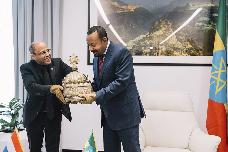 Ethiopia's Prime Minister, Abiy Ahmed, right, with gloved hands as he officially hands over a crown to the country's tourism minister, Hirut Kassaw, Thursday, Feb. 20, 2020.  The 18th Century Ethiopian crown has been returned home after being hidden in a Dutch flat for the past 21-years. (The Office of Prime Minister Abiy Ahmed via AP)