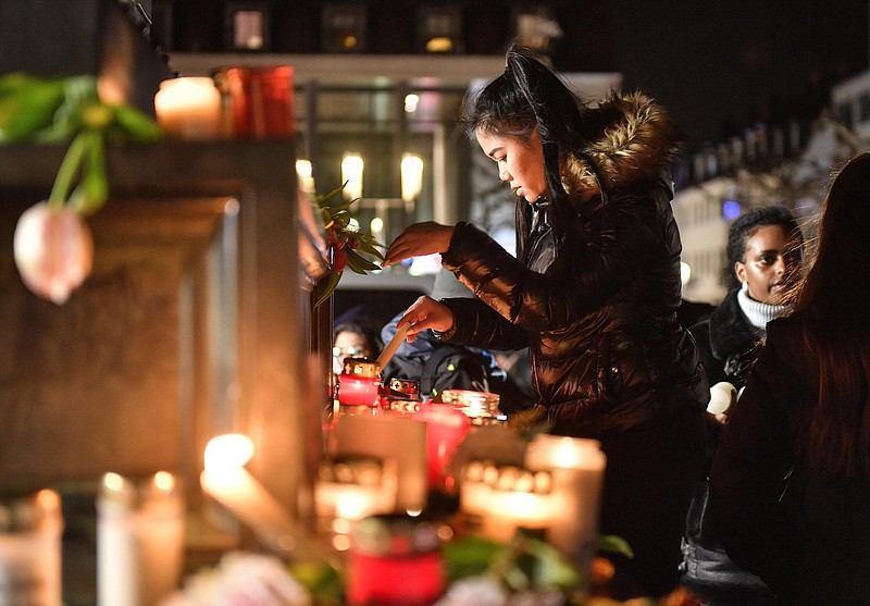 A woman lights a candle at a monument on the market place during a mourning for the victims of the shooting in Hanau, Germany, Thursday, Feb. 20, 2020. A 43-year-old German man shot and killed nine people at several locations in a Frankfurt suburb overnight in attacks that appear to have been motivated by far-right beliefs, officials said Thursday. (AP Photo/Martin Meissner)