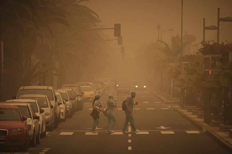 People in carnival dress walk across a street crossing in a cloud of red dust in Santa Cruz de Tenerife, Spain, Sunday, Feb. 23, 2020. Flights leaving Tenerife have been affected after storms of red sand from Africa's Saharan desert hit the Canary Islands and carnival was finally cancelled it was announced. (AP Photo/Andres Gutierrez)