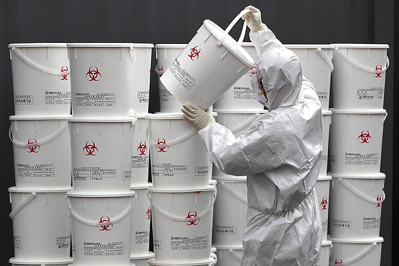 A worker in protective gear stacks plastic buckets containing medical waste from coronavirus patients at a medical center in Daegu, South Korea, Monday, Feb. 24, 2020. South Korea reported another large jump in new virus cases Monday a day after the the president called for "unprecedented, powerful" steps to combat the outbreak that is increasingly confounding attempts to stop the spread. (Lee Moo-ryul/Newsis via AP)