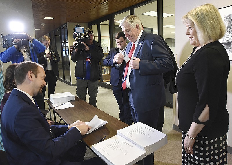 As first lady Teresa Parson, right, looks on, Gov. Mike Parson retrieves his drivers license to show Adam Trowbridge, seated at left, and Darcie Rehagen, as he files the proper paperwork to run for his current political seat. Trowbridge and Rehagen work for the Secretary of State's office.