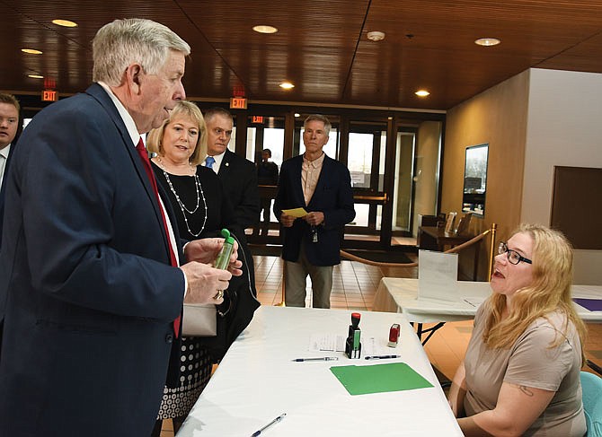 Gov. Mike Parson uses hand sanitizer Tuesday as he and first lady Teresa Parson, second from left, make their way through the line at the Secretary of State's office. Kelly Pointer, seated, with the Department of Revenue, had the bottle for anyone to use. 