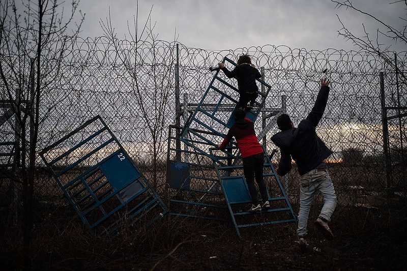 A migrant, right, throws a stone to the Greek riot police as other two migrants climbing on a border fence at the Turkish-Greek border in Pazarkule, Edirne region, Turkey, on Friday, March 6, 2020. Clashes erupted anew on the Greek-Turkish border as migrants attempted to push through into Greece, while the European Union's foreign ministers held an emergency meeting to discuss the situation on the border and in Syria, where Turkish troops are fighting. (AP Photo/Felipe Dana)