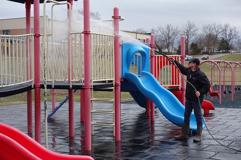 Carson Shackelford power washes playground equipment with 200 degree water.