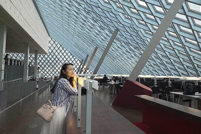 In this August 2019, photo released by Florian Hayek, Courtney Huang, a Chinese citizen living and working in the United States, poses for a photo in the Central Library in Seattle, Wa. Huang is one of hundreds of Chinese whose jobs, lives, and right to work in the U.S. are on the line after the Trump administration imposed a travel ban and visa processing halt on foreigners in China over the coronavirus outbreak. Huang, who aspires to become a U.S. citizen, is worried that she could lose her job and her right to live in the States because her work visa wasn't issued due to the halt. (Florian Hayek via AP)