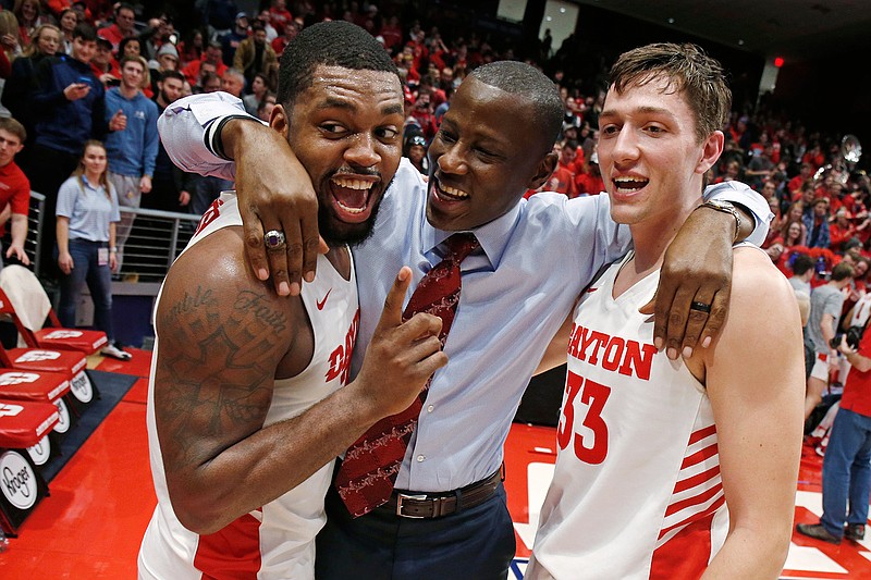 In this Feb. Feb. 28, 2020, file photo, Dayton coach Anthony Grant, center, gives a hug to players Trey Landers, left, and Ryan Mikesell following the team's 82-67 win over Davidson in an NCAA college basketball game in Dayton, Ohio. The coronavirus outbreak has abruptly roused the University of Dayton from its dream of a basketball season. The 29-2 Flyers were rolling into tournament play on a 20-game winning streak that had lifted spirits in an Ohio city battered in the past year by violent deaths and devastation. The NCAA decision to cancel March Madness ended hopes for the small Roman Catholic school's first Final Four appearance in 53 years. (AP Photo/Gary Landers, File)