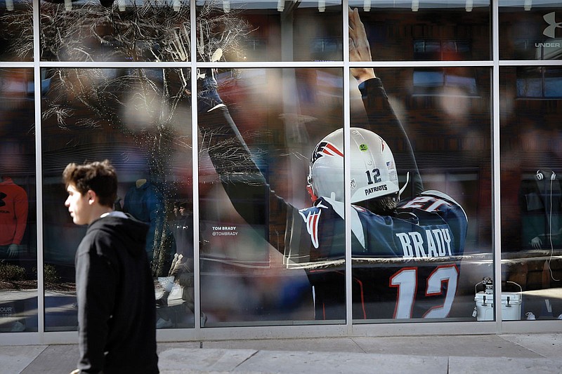 A passer-by walks past an oversized photograph of former Patriots quarterback Tom Brady on Wednesday at Patriot Place mall in Foxborough, Mass. Brady agreed to a two-year, $50 million contract with the Buccaneers.