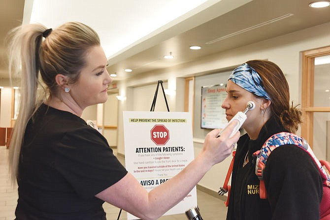 Brittany Baines takes the temperature of nurse Taylor Howard on Friday morning at Capital Region Medical Center. Baines is corporate and community health coordinator at the hospital. CRMC has announced visitor restrictions effective immediately due to the spread of COVID-19.