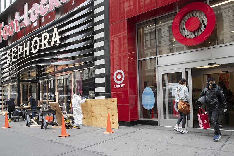 FILE - In this Friday, March 20, 2020 file photo, a shopper leaves the Target Store on 34th St. with supplies as carpenter board up the Sephora story in New York.  Target Corp. said Friday it will give a $2 an hour wage increase to its 300,000-plus workers who have been scrambling to help customers. The pay bump will be effective at least through May 2. (AP Photo/Mary Altaffer, File)