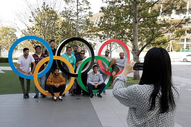 A group of students from Uruguay pose for a souvenir picture on the Olympic Rings outside the Olympic Stadium in Tokyo on Saturday. The Olympic flame from Greece arrived Friday in Japan, even as the opening of the the Tokyo Games in four months is in doubt with more voices suggesting the games should to be postponed or canceled because of the worldwide coronavirus pandemic.