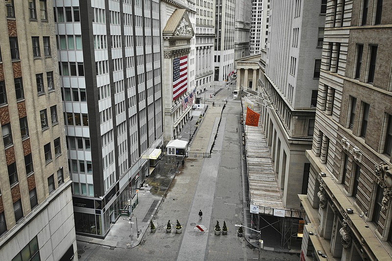 FILE - In this Saturday, March 21, 2020 file photo, a lone pedestrian wearing a protective mask walks past the New York Stock Exchange as coronavirus concerns empty a typically bustling downtown area in New York. Stocks around the world swung lower Monday, March 23 even after the Federal Reserve announced a tidal wave of support for lending markets, going way beyond the “bazooka” it had already unloaded.   (AP Photo/John Minchillo, File)