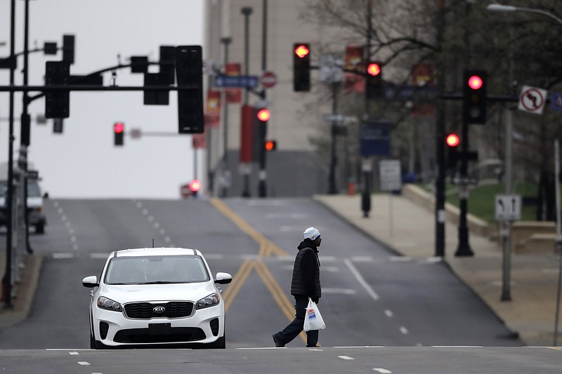 A man carries a bag of groceries through downtown Kansas City, Mo. Sunday, March 22, 2020. Officials in Missouri's largest cities are ordering a mandatory stay-at-home rule to residents starting next week in an effort to slow the spread of the coronavirus. St. Louis and St. Louis County authorities first announced the order, which is to begin Monday, before Kansas City officials followed later Saturday with a similar order. The order in Kansas City and surrounding areas is set to begin Tuesday. (AP Photo/Charlie Riedel)