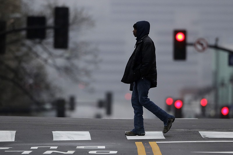 A person crosses a near-empty downtown street in Kansas City, Mo. Sunday, March 22, 2020. (AP Photo/Charlie Riedel)
