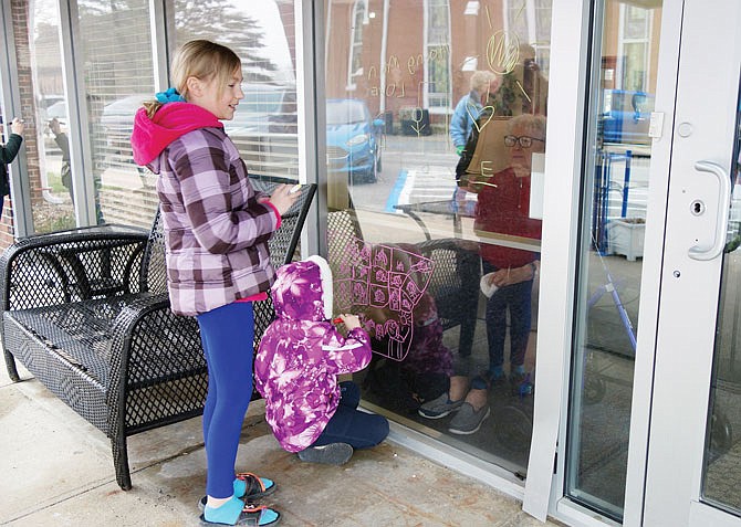 Sisters Bella and Molly Yates draw pictures and play tic-tac-toe with a resident of Fulton Presbyterian Manor. Several families visited Wednesday to safely bring cheer to residents.