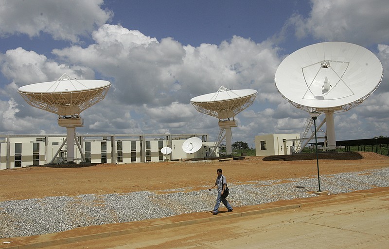 FILE - In this Oct. 28, 2008 file photo, a man walks past a satellite dish station in El Sombrero, Venezuela. Venezuela’s only telecommunications satellite has veered off its orbit and stopped working, according to a government statement on March 26, 2020.  (AP Photo/Howard Yanes, File)