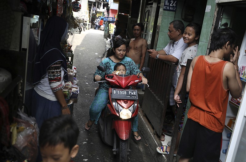 A motorist rides past as residents talk on an alley at a low-income neighborhood in Jakarta, Indonesia, March 23, 2020. As the virus spreads, the World Health Organization has pointed out that the future of the pandemic will be determined by what happens in some of the world’s poorest and most densely populated countries. From Mumbai to Rio de Janeiro to Johannesburg the question is: What do you do if there is no space to socially distance yourself from others in some of world’s most unequal regions? (AP Photo/Dita Alangkara)