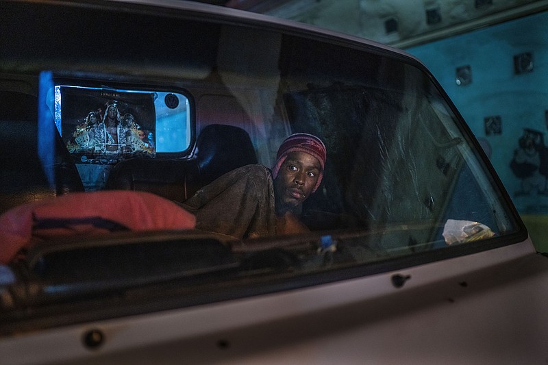 A man living in his car reacts to police and army patrolling downtown Johannesburg, South Africa, Friday, March 27, 2020. Police and army started patrolling moments after South Africa went into a nationwide lockdown for three weeks in an effort to mitigate the spread to the coronavirus. The new coronavirus causes mild or moderate symptoms for most people, but for some, especially older adults and people with existing health problems, it can cause more severe illness or death.(AP Photo/Jerome Delay)