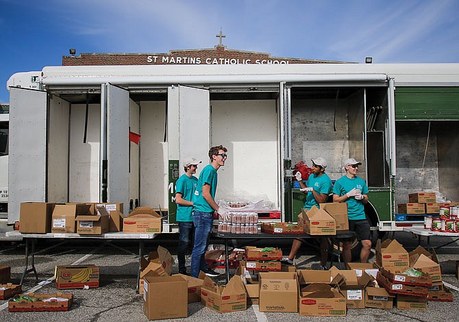 Helias Catholic High School students and Catholic Charities volunteers Connor McDaniel, Logan Mathews, Daniel Dusenberg and Jonathan Dolan chat Wednesday while unloading the last few food items from a mobile food pantry at St. Martins Catholic School.