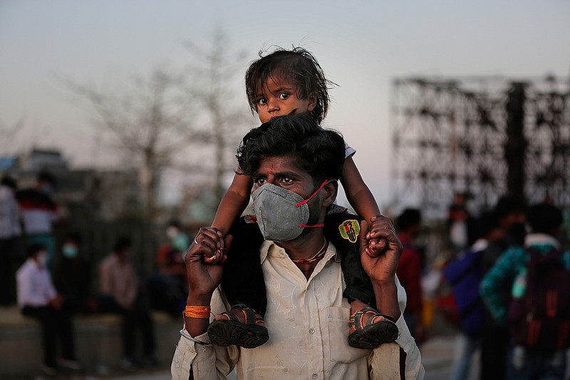 An Indian migrant worker carries a child on his shoulders as they wait for transportation to their village following a lockdown amid concern over spread of coronavirus in New Delhi, India, Saturday, March 28, 2020. Authorities sent a fleet of buses to the outskirts of India's capital on Saturday to meet an exodus of migrant workers desperately trying to reach their home villages during the world's largest coronavirus lockdown. Thousands of people, mostly young male day laborers but also families, fled their New Delhi homes after Prime Minister Narendra Modi announced a 21-day lockdown that began on Wednesday and effectively put millions of Indians who live off daily earnings out of work. (AP Photo/Altaf Qadri)