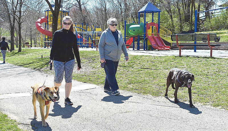 From left, Carol Scott and her dog Cayman, along with Abbie McFerron and her dog, Brady, take a walk Sunday at McKay Park. An empty, taped-off playground is in the background. Officials say that even with a county stay-at-home order, it's still important to get out for exercise and recreation.