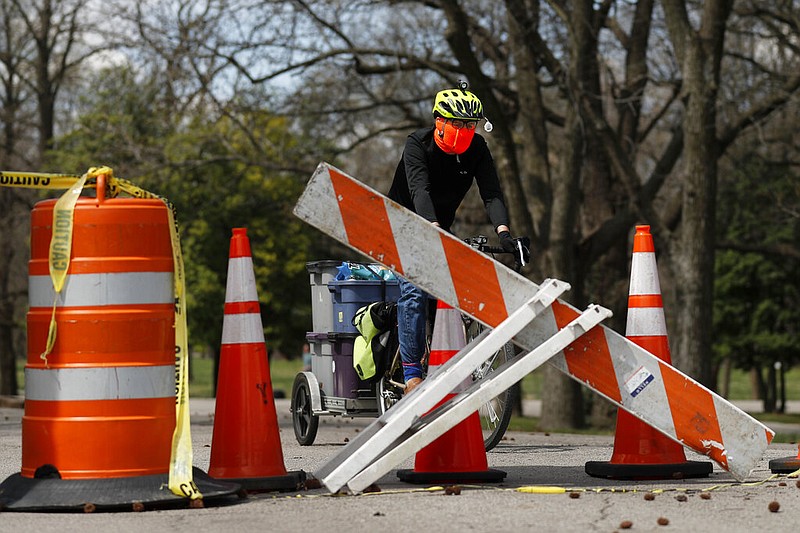 A person rides a bike past barricades at an entrance to Tower Grove Park Tuesday, March 31, 2020, in St. Louis. The entrance to the park has been closed to vehicle traffic in an effort to give visitors on foot more room to practice social distancing and help slow the spread of the coronavirus. (AP Photo/Jeff Roberson)