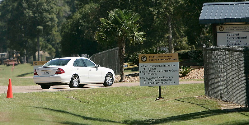 In this Sept. 26, 2006, file photo a person drive through the gates of a federal prison in Oakdale, La. The federal Bureau of Prisons is locking all its 146,000 inmates in their cells for the next two weeks in an unparalleled effort to slow the spread of the coronavirus, as the focus shifts to the Louisiana compound, where two inmates have died and nearly 20 others remain hospitalized. (AP Photo/Rogelio V. Solis, File)