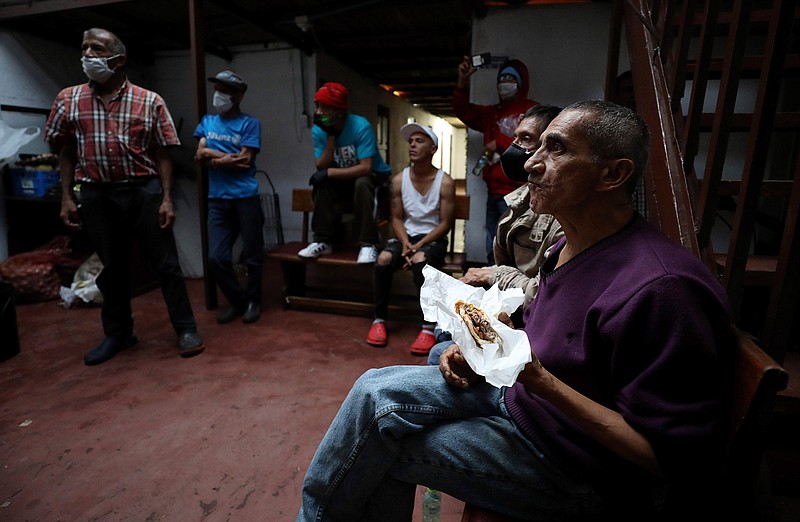 An elderly man eats a hamburger that was donated by Emiliano Moscoso in a boarding house in Bogota, Colombia, Monday, March 30, 2020. Moscoso recently launched a program called "Solidarity Menu" to feed people in need during the coronavirus outbreak . (AP Photo/Fernando Vergara)