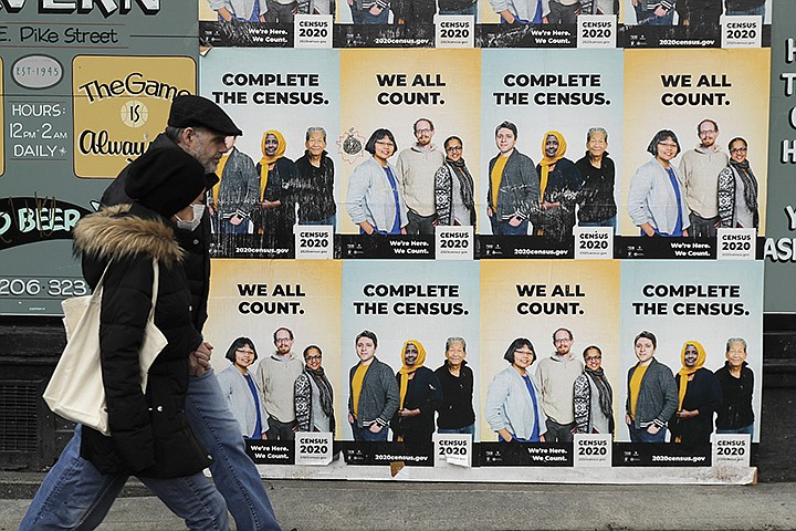 People walk past posters encouraging participation in the 2020 Census, Wednesday, April 1, 2020, in Seattle's Capitol Hill neighborhood. Wednesday is Census Day, the date used to reference where a person lives for the once-a-decade count, as the U.S. is almost paralyzed by the spread of the novel coronavirus, but census officials vowed the job would be completed by its year-end deadline. (AP Photo/Ted S. Warren)