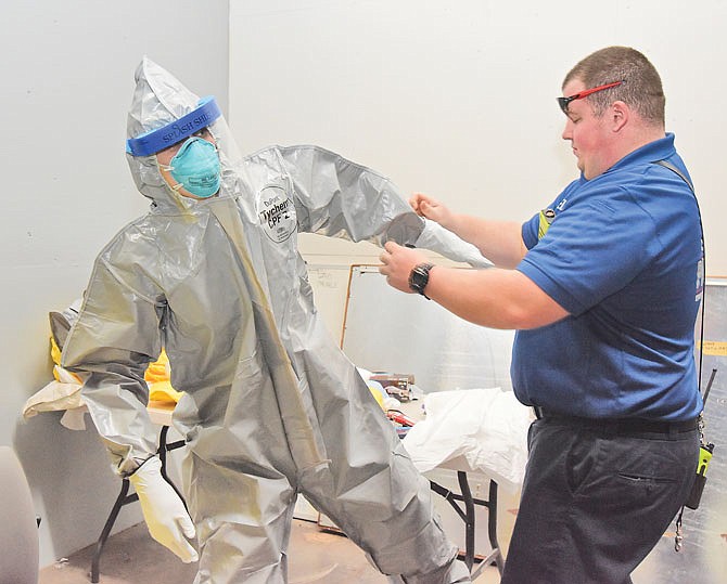 Cole County EMS paramedic Nicholas Barton, right, assists fellow paramedic Cpt. Kelly Holman on Thursday as she demonstrates personal protective equipment at the Southridge Drive station house. This particular gear is from when emergency personnel were gearing up for the Ebola virus and has enclosed foot protection. 