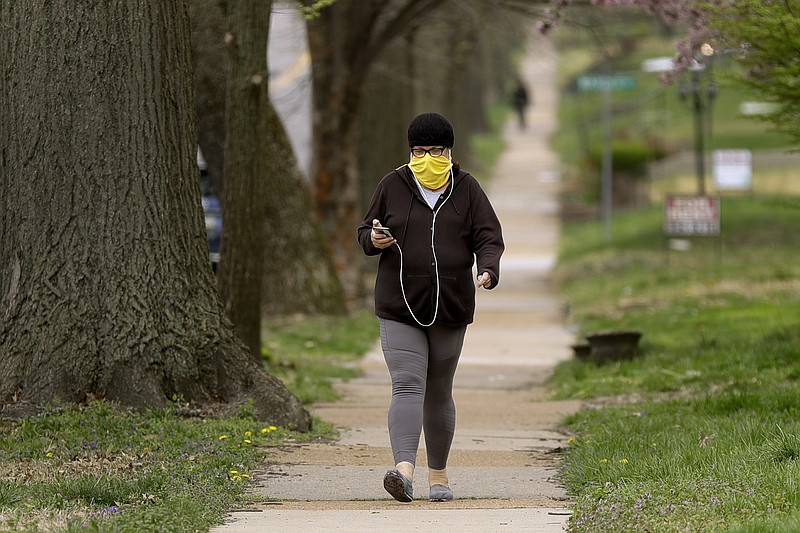 A person covers their face with a scarf while walking down the street Monday, April 6, 2020, in University City, Mo. The Centers for Disease Control and Prevention now recommends wearing cloth face coverings in public settings after recent studies have shown a significant portion of the population can transmit the coronavirus without showing any symptoms. (AP Photo/Jeff Roberson)