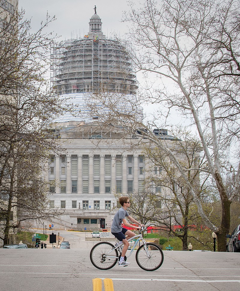 The Capitol is seen in the background Monday as Nick Ammons crosses Capitol Avenue while riding his bicycle. While the Capitol is technically still open, state leaders are asking the public to refrain from visiting the building while they return this week to cast votes.
