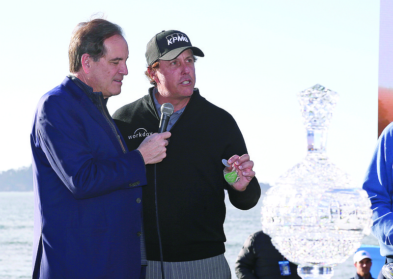 In this Feb. 11, 2019, file photo, while being interviewed by broadcaster Jim Nantz (left), Phil Mickelson holds up a silver dollar that belonged to his grandfather during an awards ceremony on the 18th green of the Pebble Beach Golf Links after winning the AT&T Pebble Beach Pro-Am in Pebble Beach, Calif.