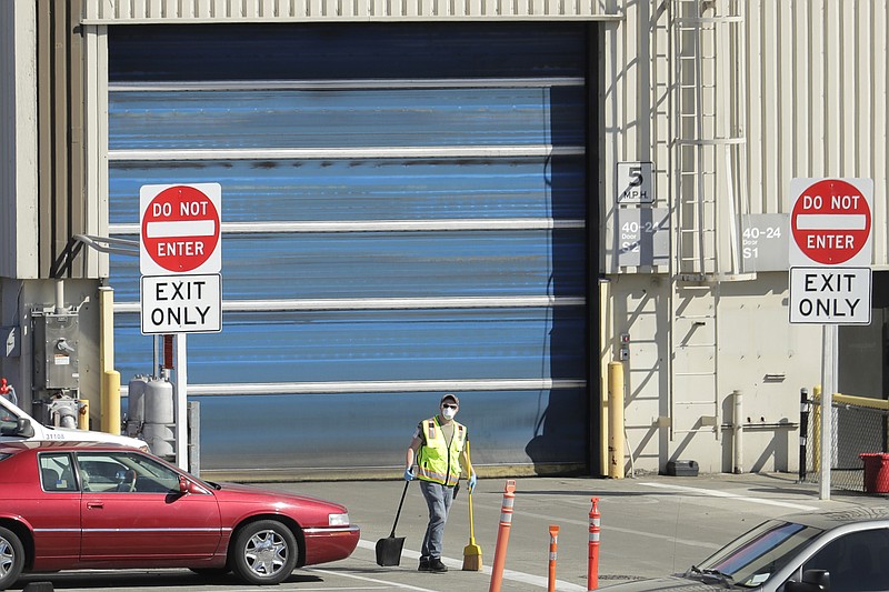 FILE - In this April 13, 2020 file photo, a worker wears a mask as he cleans up an area outside an entrance at Boeing Co.'s airplane assembly facility in Everett, Wash., north of Seattle.  American industry collapsed in March as the coronavirus pandemic wreaked havoc on the U.S. economy. Manufacturing and overall industrial production posted the biggest drops since the United States demobilized after World War II.  (AP Photo/Ted S. Warren, File)