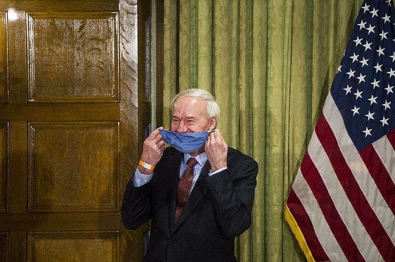 In this April file photo, Arkansas Gov. Asa Hutchinson laughs and puts on his mask after hiscoronavirus update at the state Capitol.(Arkansas Democrat-Gazette/Stephen Swofford)