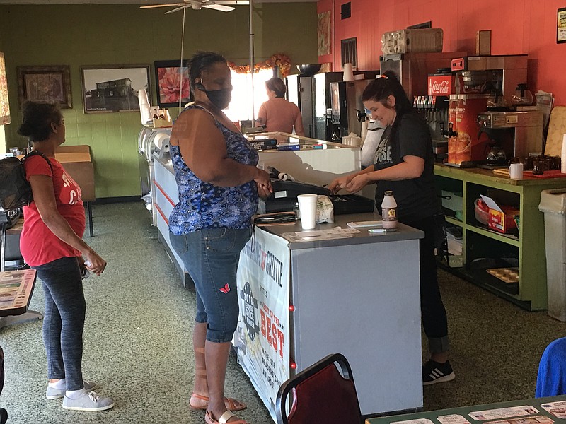  Cashier Brittany Gregory, checks out customer Marchall Brown, who is wearing a protective mask, which is so common now. Behind her is Kathaleen Franklin. In the background, working the drive-through window, is Anna Allgor, who owns the business with her husband.