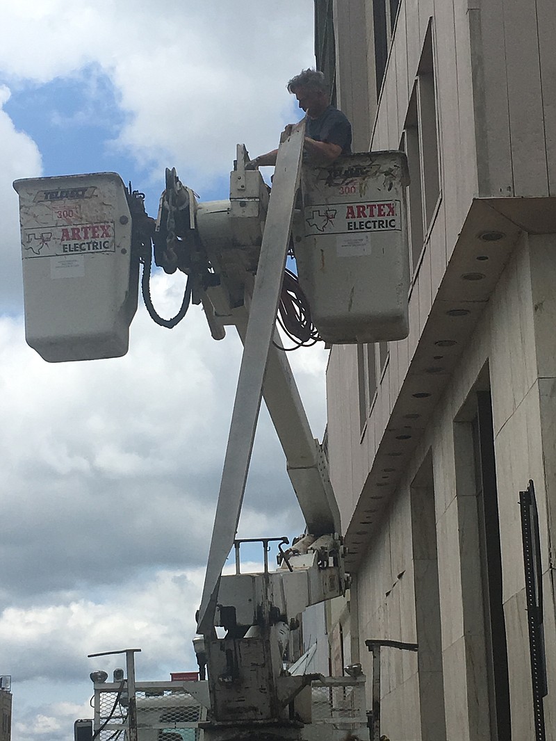 Developer David Peavy in a bucket truck takes down a strip of siding on a historic downtown bank Friday evening. Underneath are architectural ornaments that Peavy and his group will restore when they remove the facade, put on in about 1970, covering the eight-story brick building. (Staff photo by Les Minor)