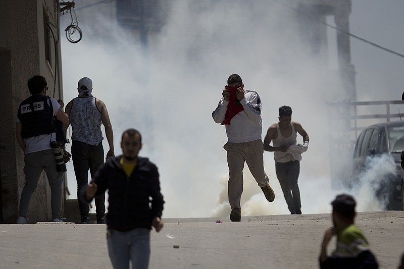 Palestinians run away from tear gas fired by Israeli soldiers during clashes after a soldier was killed when a rock thrown off a rooftop struck him in the head g during an arrest raid, in the village of Yabad near the West Bank city of Jenin, Tuesday, May. 12, 2020. Tuesday's raid was aimed at arresting four Palestinians wanted for stone-throwing at Israeli vehicles and other recent attacks. (AP Photo/Majdi Mohammed)