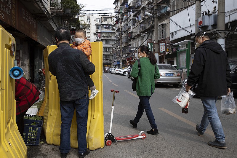 In this photo taken Wednesday, April 1, 2020, residents walk past a sealed off neighborhood in Wuhan, central China's Hubei province. Authorities in Wuhan, the Chinese city where the coronavirus pandemic first broke out, have reportedly launched a plan to test everyone in the city of 11 million people in the next 10 days. (AP Photo/Ng Han Guan)
