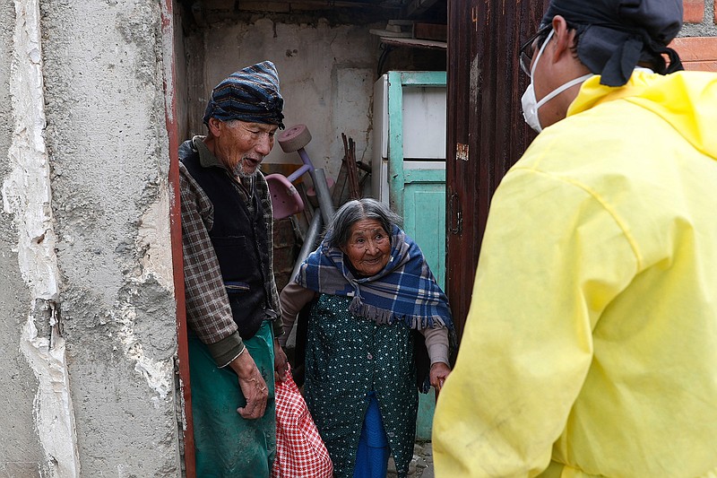 In this May 6, 2020 photo, 85-year-old Francisco Huayta and his wife, 93-year-old Guillermina Chumacero, speak with an "Adopt a Grandparent" volunteer after he delivered a bag of donated food to their home, in La Paz, Bolivia. The campaign urges volunteers to help senior citizens if they need safe support. So far, about 20 young people have offered to help. (AP Photo/Juan Karita)