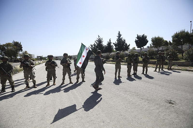 A man carries Syrian Independence flag as Turkish soldiers block a road after a nearby explosion outside the city of Ariha, in Idlib province, Syria, Tuesday, May 12, 2020. (AP Photo/Ghaith Alsayed)