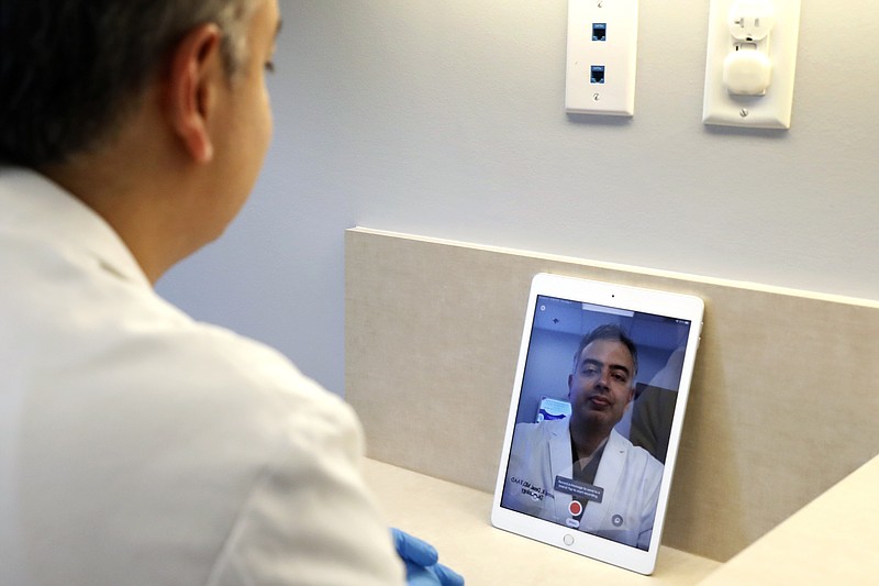 Dermatologist Dr. Seemal Desai poses for a photo in an examination room in his office in Plano, Texas, Thursday, May 7, 2020. Desai uses the privacy of an examination room and a tablet computer to virtually visit with some of his patients. (AP Photo/Tony Gutierrez)