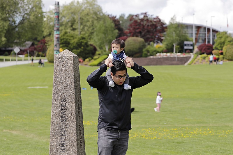 In this photo taken Sunday, May 17, 2020, Bryan Albano, walks with his son Zachary atop his shoulders in Canada at Peace Arch Provincial Park, adjacent to Peace Arch Historical State Park on the U.S. side, where people can walk freely between the two countries at an otherwise closed border, in Blaine, Wash. Canada and the U.S. have agreed to extend their agreement to keep the border closed to non-essential travel to June 21 during the coronavirus pandemic. The restrictions were announced on March 18, were extended in April and now extended by another 30 days. (AP Photo/Elaine Thompson)