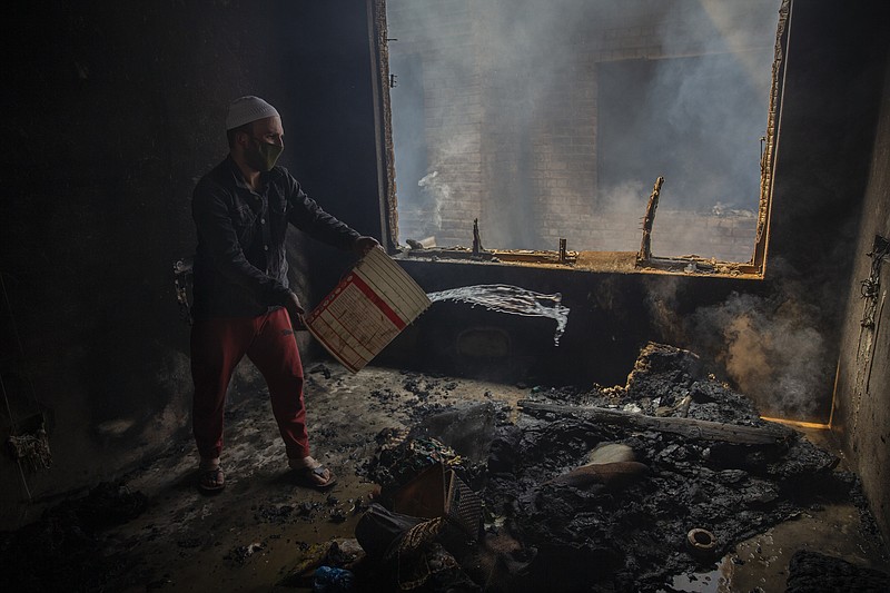 A Kashmiri man douses a fire in a house which was damaged in a gun-battle in Srinagar, Indian controlled Kashmir, Tuesday, May 19, 2020. Indian government forces killed two rebels in disputed Kashmir on Tuesday and shut down cellphone and mobile internet services during subsequent anti-India protests, officials and residents said. (AP Photo/ Dar Yasin)